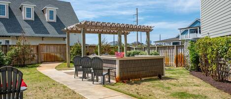 Un patio trasero con una pérgola de madera, zona de barbacoa y un conjunto de asientos.