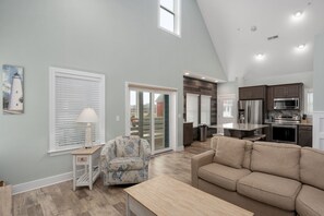 A modern living room with a sofa, a chair, a lamp, and a kitchen area with appliances. - Ocracoke Cottage: Semi-Oceanfront, Hot Tub, Close walk to the Beach (Nags Head)
