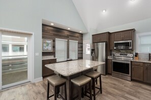 A modern kitchen with a central island, stainless steel appliances, and a view to the outside.