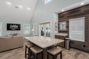 A modern kitchen with a granite island, wooden flooring, and a large window with blinds.