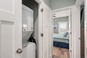 A laundry room with a washer and dryer, a hallway leading to a bedroom with a bed and a window.