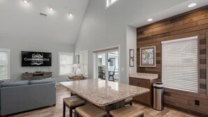 Une cuisine moderne dotée d’un grand îlot central, de touches de bois et d’un téléviseur à écran plat diffusant des images de «Vacances à Coastal Carolina».
