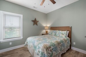 A bedroom with a bed, a starfish decoration, a nightstand with a lamp, and a ceiling fan.