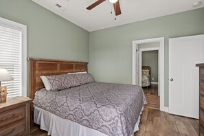 A bedroom with a wooden headboard, a patterned bedspread, a nightstand, and a ceiling fan.