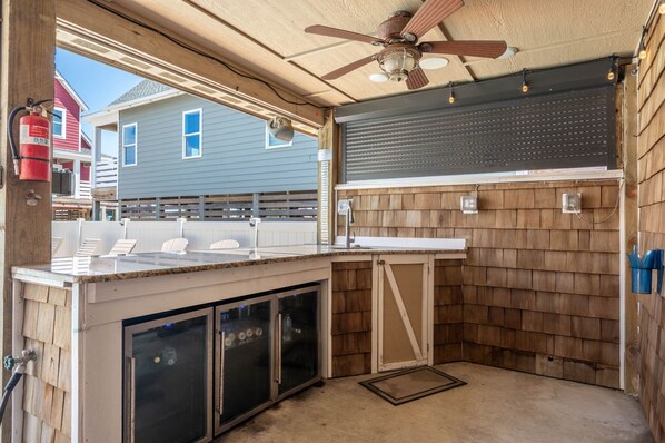 A covered outdoor kitchen area with a ceiling fan, built-in cabinets, and a view of neighboring houses.