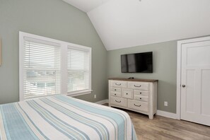 Une chambre à coucher avec un lit, une commode, un téléviseur et une porte.