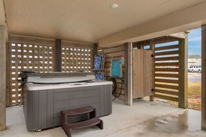 Banheira de hidromassagem sob uma pérgola de madeira, com vista para um parque de estacionamento.
