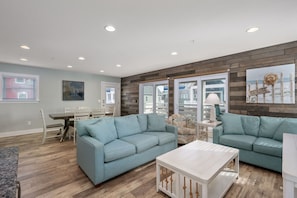A modern living room with two light blue sofas, a white coffee table, and a dining area with a white table and chairs. - Currituck Cottage: Semi-Oceanfront, Private Hot Tub, Community Pool Access! (Nags Head)