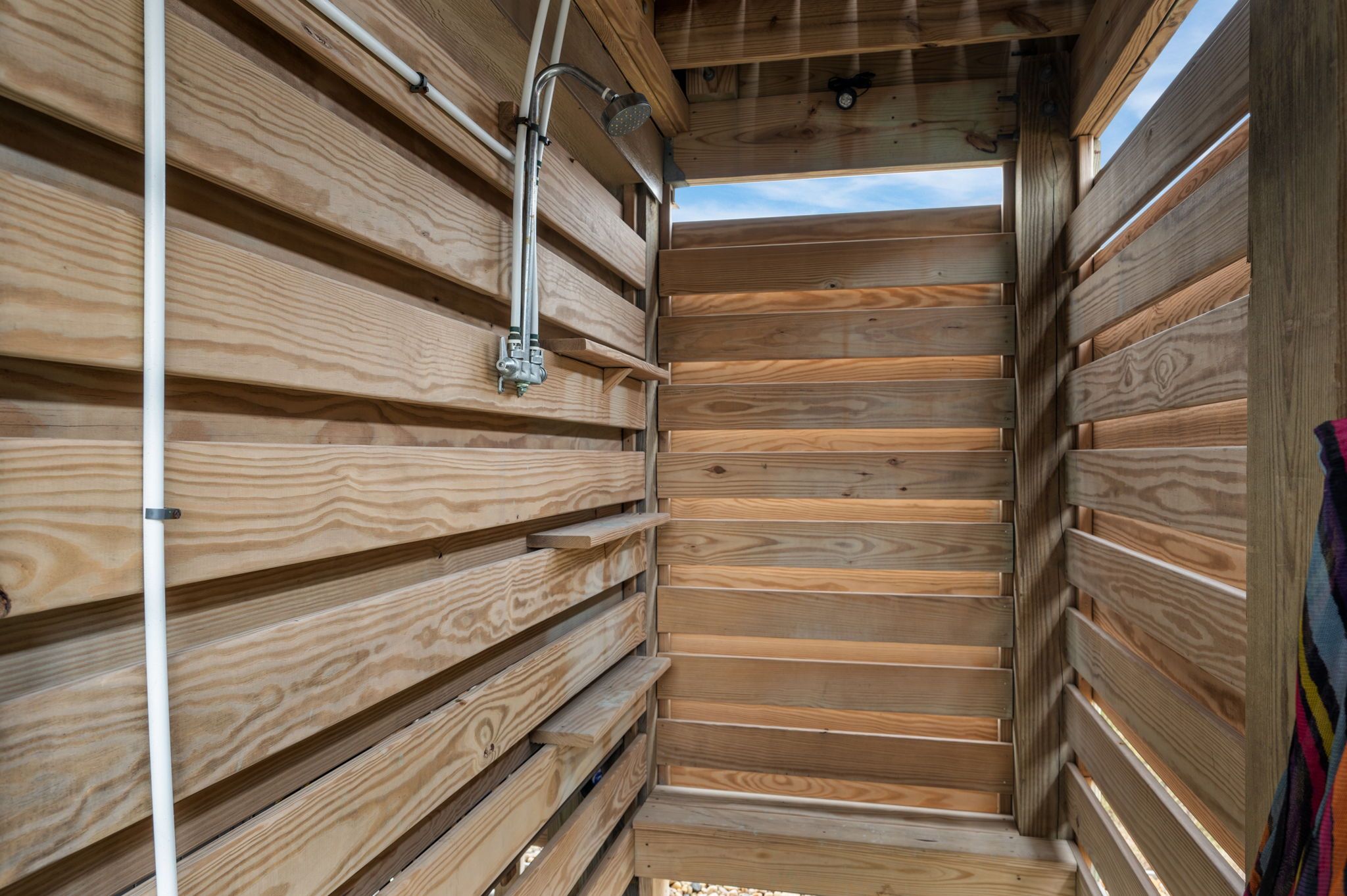 A wooden interior with horizontal slats, a metal shower fixture, and a window allowing natural light.