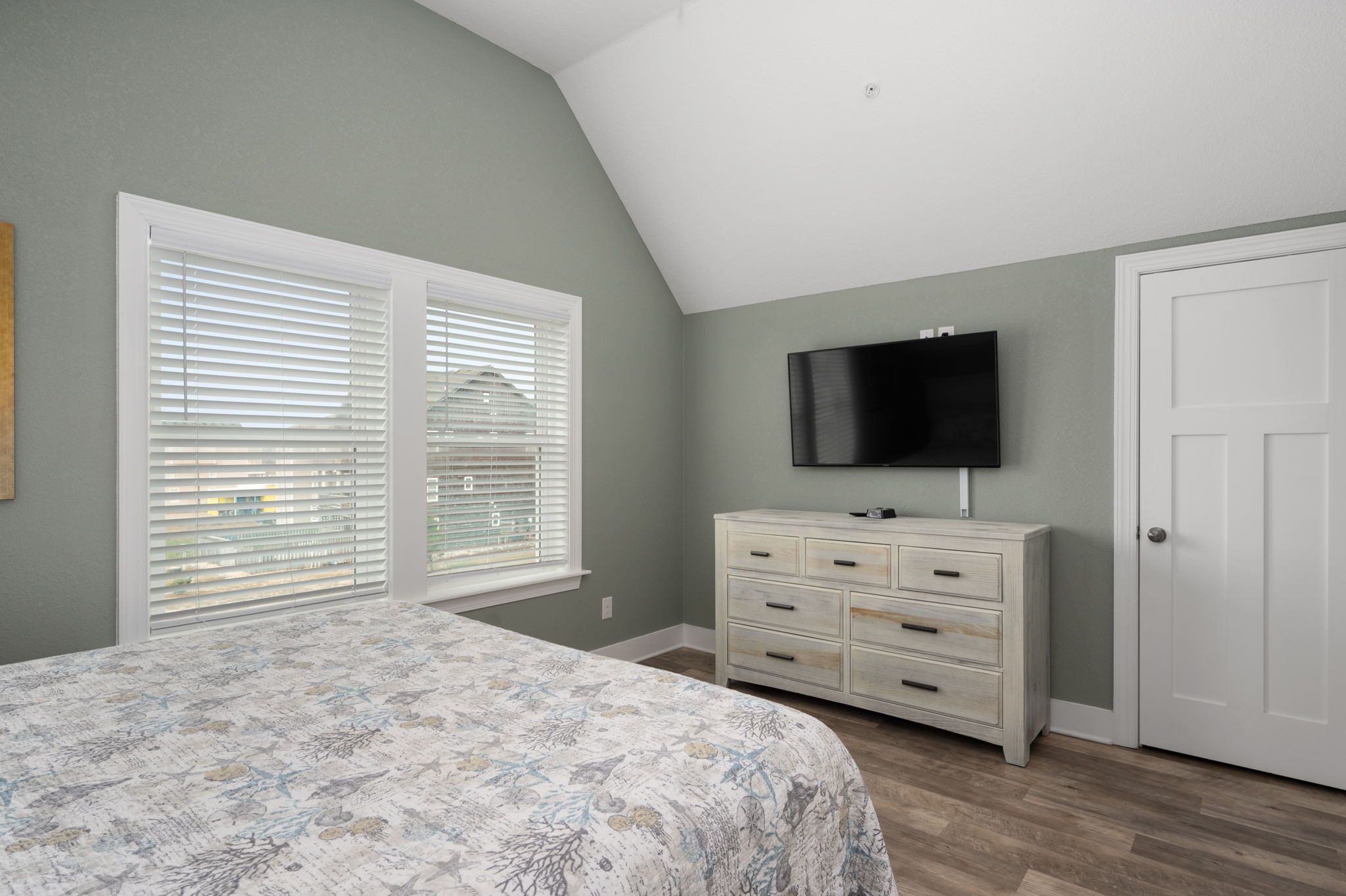 A bedroom with a bed, a dresser, a television, and a door.
