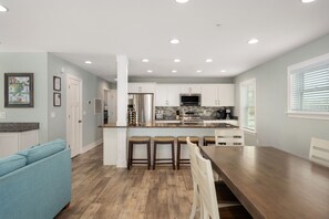 Une cuisine moderne avec des meubles blancs, un îlot central et un coin repas comprenant une table en bois et des tabourets de bar.