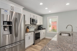 A modern kitchen with stainless steel appliances, a granite countertop, and a window with blinds. - Currituck Cottage: Semi-Oceanfront, Private Hot Tub, Community Pool Access! (Nags Head)