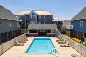 A swimming pool with lounge chairs and a covered seating area, surrounded by multi-story buildings with balconies. - Currituck Cottage: Semi-Oceanfront, Private Hot Tub, Community Pool Access! (Nags Head)
