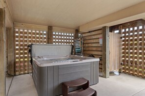 A hot tub in a covered outdoor area with wooden walls and a metal gate.