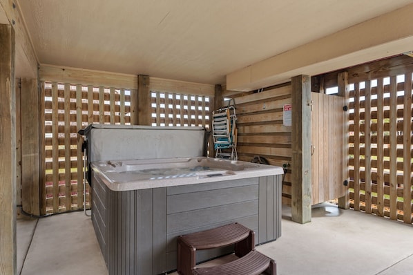 A hot tub in a covered outdoor area with wooden walls and a metal gate.