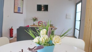 Une table à manger avec un vase de fleurs, un extincteur, un téléviseur accroché au mur et une fenêtre.