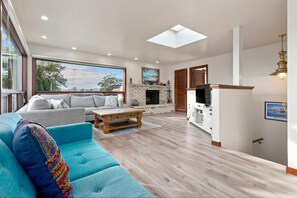 A spacious living room with a large sofa, a coffee table, and a fireplace. There is a television and a kitchen area visible. - Harbor Home - 2 blocks from the beach! (Santa Cruz)