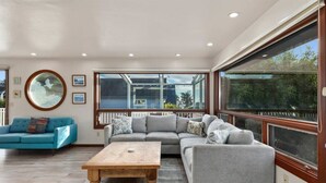A spacious living room with a large sectional sofa, a round wall hanging, and a view through large windows.