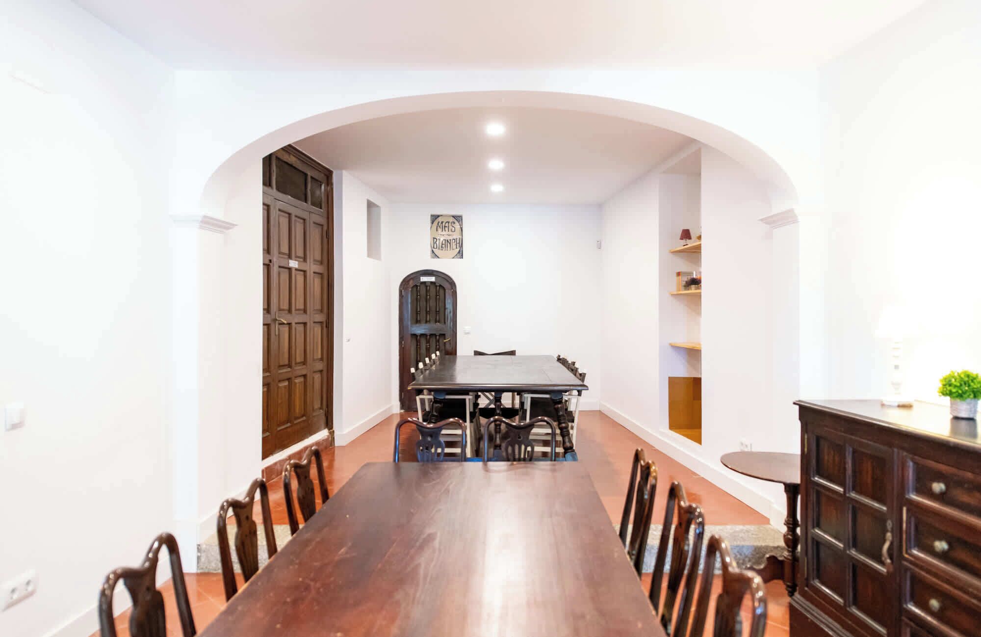 A dining area with a long wooden table and chairs, a dark wooden cabinet, and a small round table.