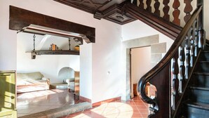 A spacious room with a bed, a chair, and a wooden staircase. - Unique 16th-Century Masia: Pool & Private Events (Barcelona)