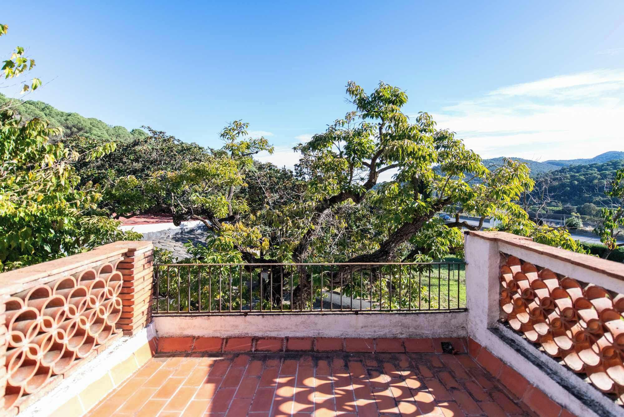 A terrace with a view of a tree and distant hills.