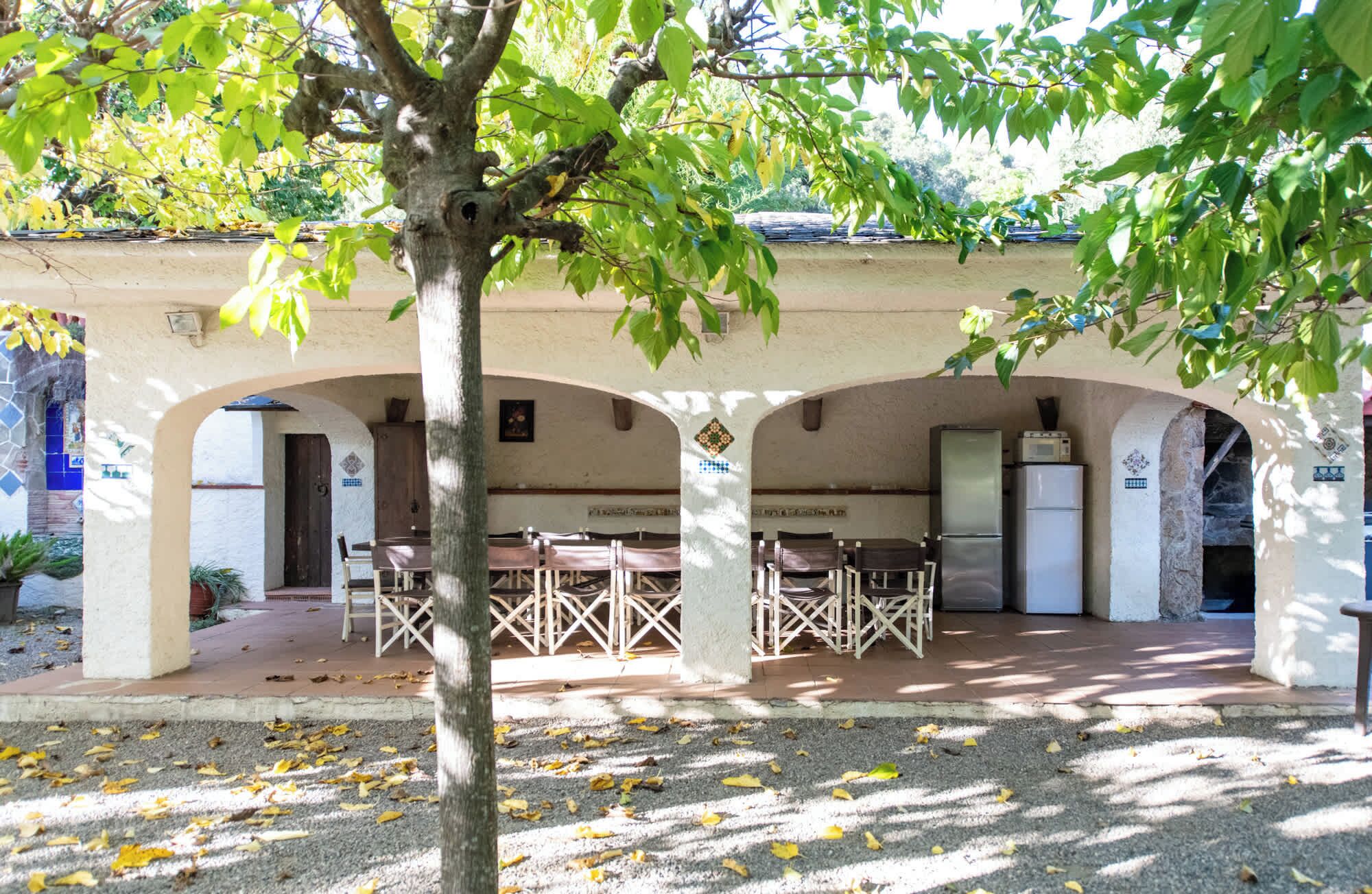 Un espacio al aire libre techado con mesas y sillas, un refrigerador y una puerta.