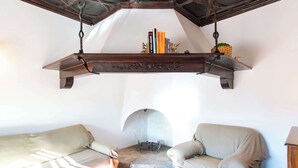A cozy room with two beige armchairs, a wooden shelf with books and decorative items, and a stone fireplace. - Unique 16th-Century Masia: Pool & Private Events (Barcelona)