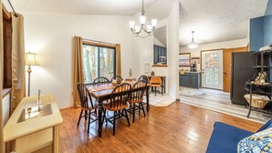 A dining area with a wooden table and chairs, a chandelier, and a view of the forest through a window. - Private Lake/Beach Cabin w/Golf, Pool, Fire pit (Terra Alta)