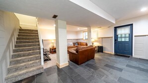 A spacious living area with a staircase, a blue door, and a leather sofa. - Private Lake/Beach Cabin w/Golf, Pool, Fire pit (Terra Alta)
