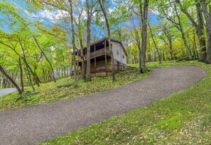 A cabin with a balcony, surrounded by trees and a gravel path.
