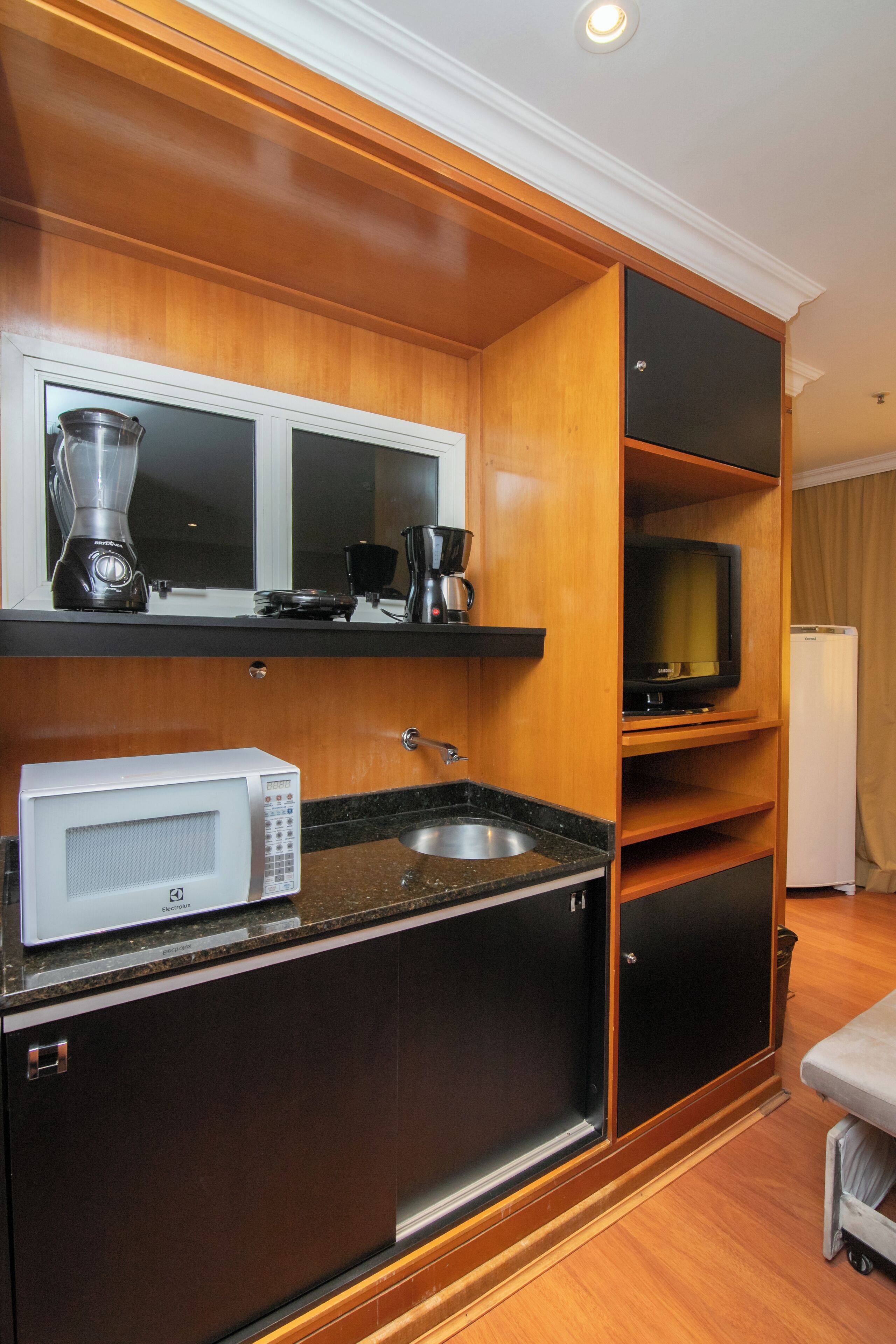 A compact kitchen with a microwave, coffee maker, and a television on a shelf.