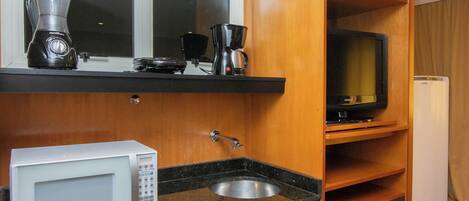 A compact kitchen with a microwave, coffee maker, and a television on a shelf.