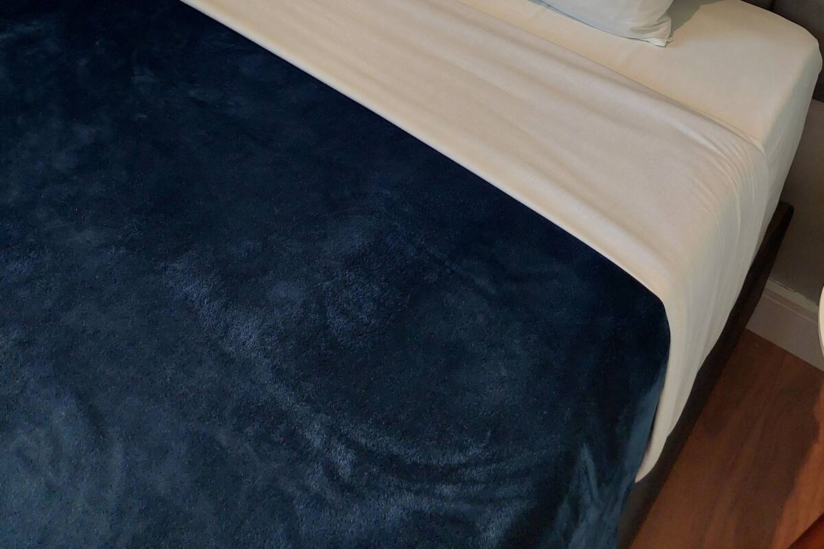 A bed with a dark blue blanket, two white pillows, and a grey upholstered headboard.