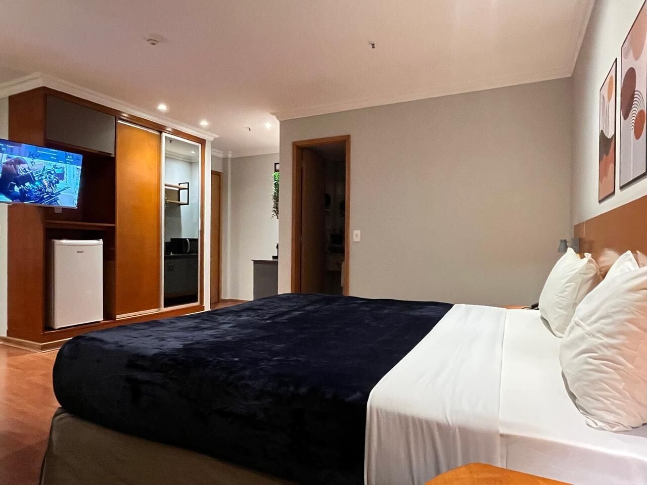 A hotel room with a bed, a TV, a mini-fridge, and a wardrobe.