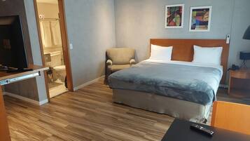 A hotel room with a bed, a chair, a desk with a TV, and a bathroom visible through an open door.