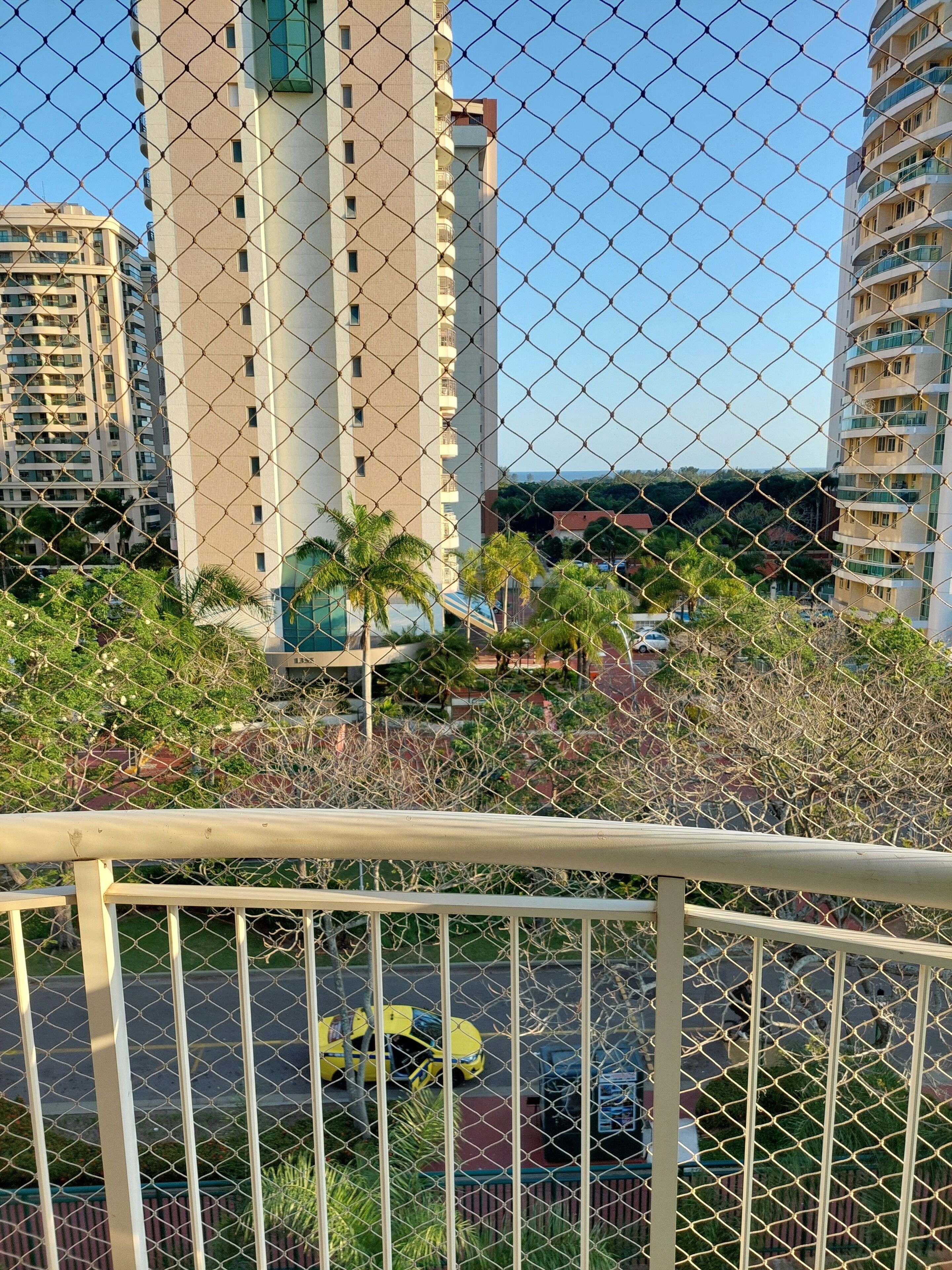 A chain-link fence with a view of tall buildings and a street with cars.