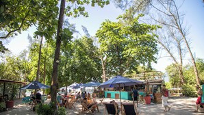 An outdoor seating area with tables and chairs under umbrellas, surrounded by trees. - Morada Stay - Flat Barra First (Rio de Janeiro)