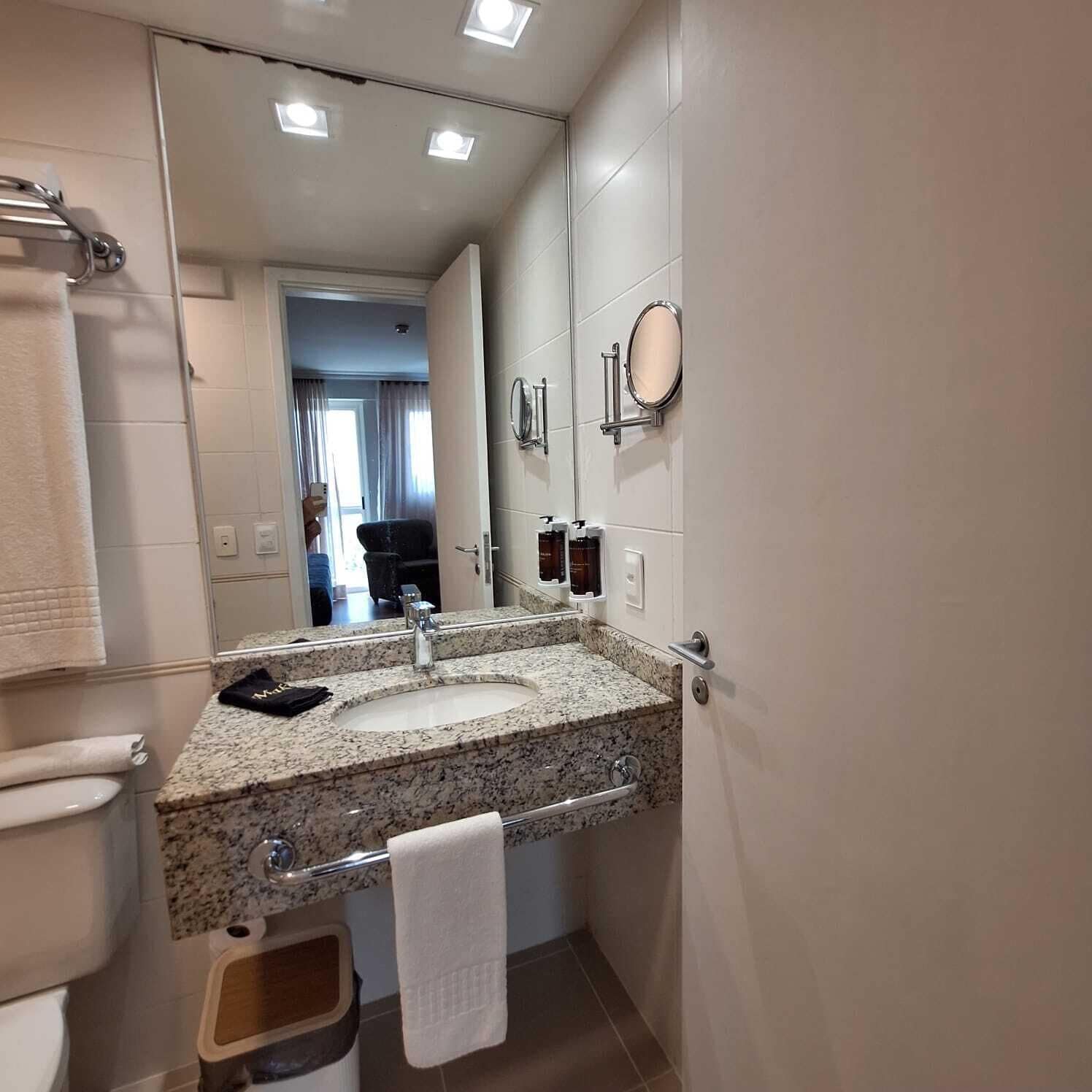 A bathroom with a granite countertop sink, a mirror, a towel rack, and a toilet.