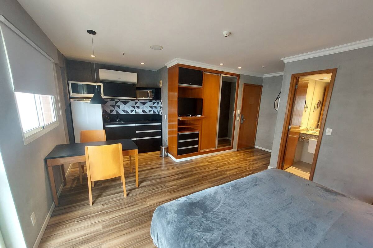 A bedroom with a bed, a desk, a chair, a wardrobe, and a kitchenette.
