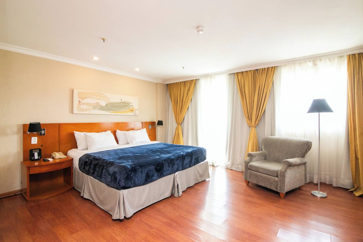 A hotel room with a large bed, a chair, a nightstand, and a lamp.