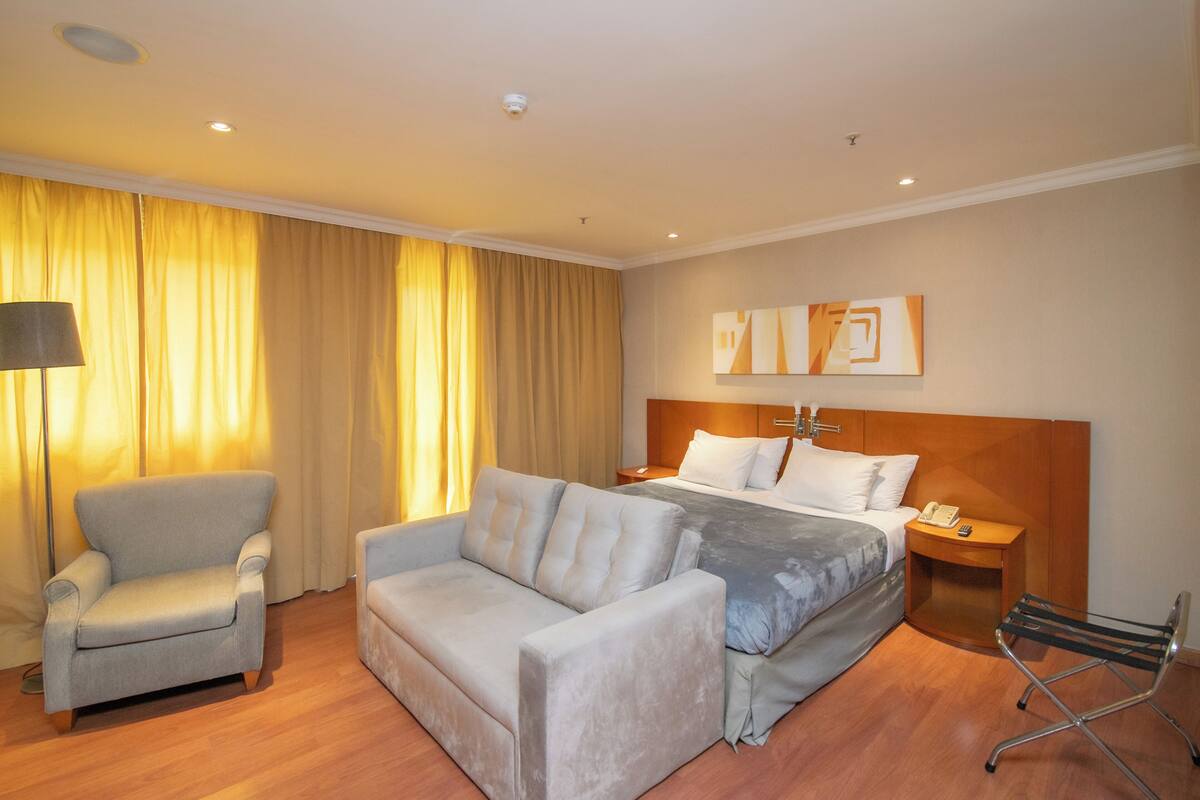 A hotel room with a bed, a sofa, a chair, and a nightstand with a phone.