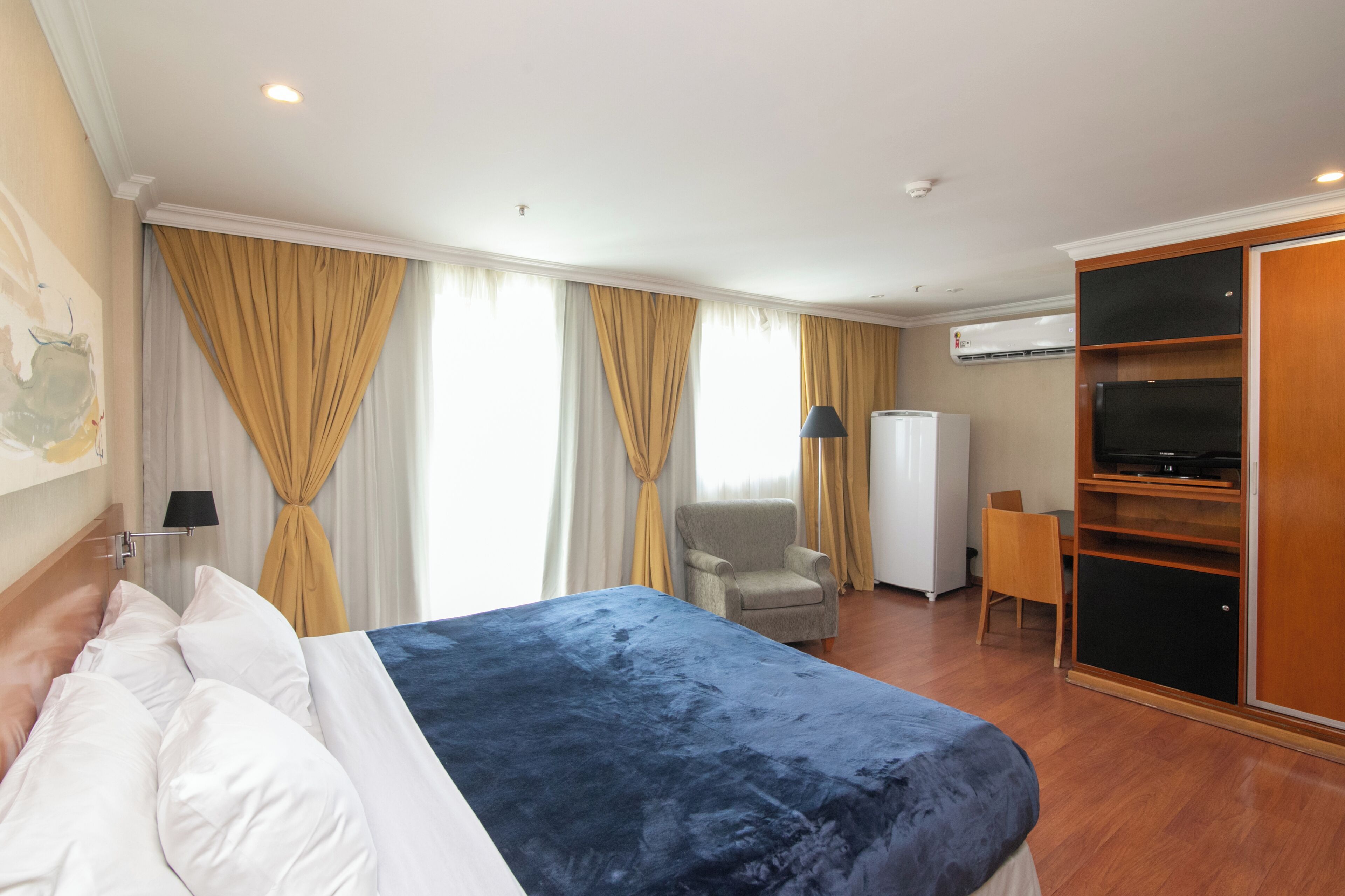 A hotel room with a bed, a chair, a TV, and a wardrobe.