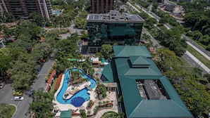 An aerial view of a hotel with a swimming pool, green-roofed buildings, and surrounding greenery. - Morada Stay - Flat Barra First (Rio de Janeiro)