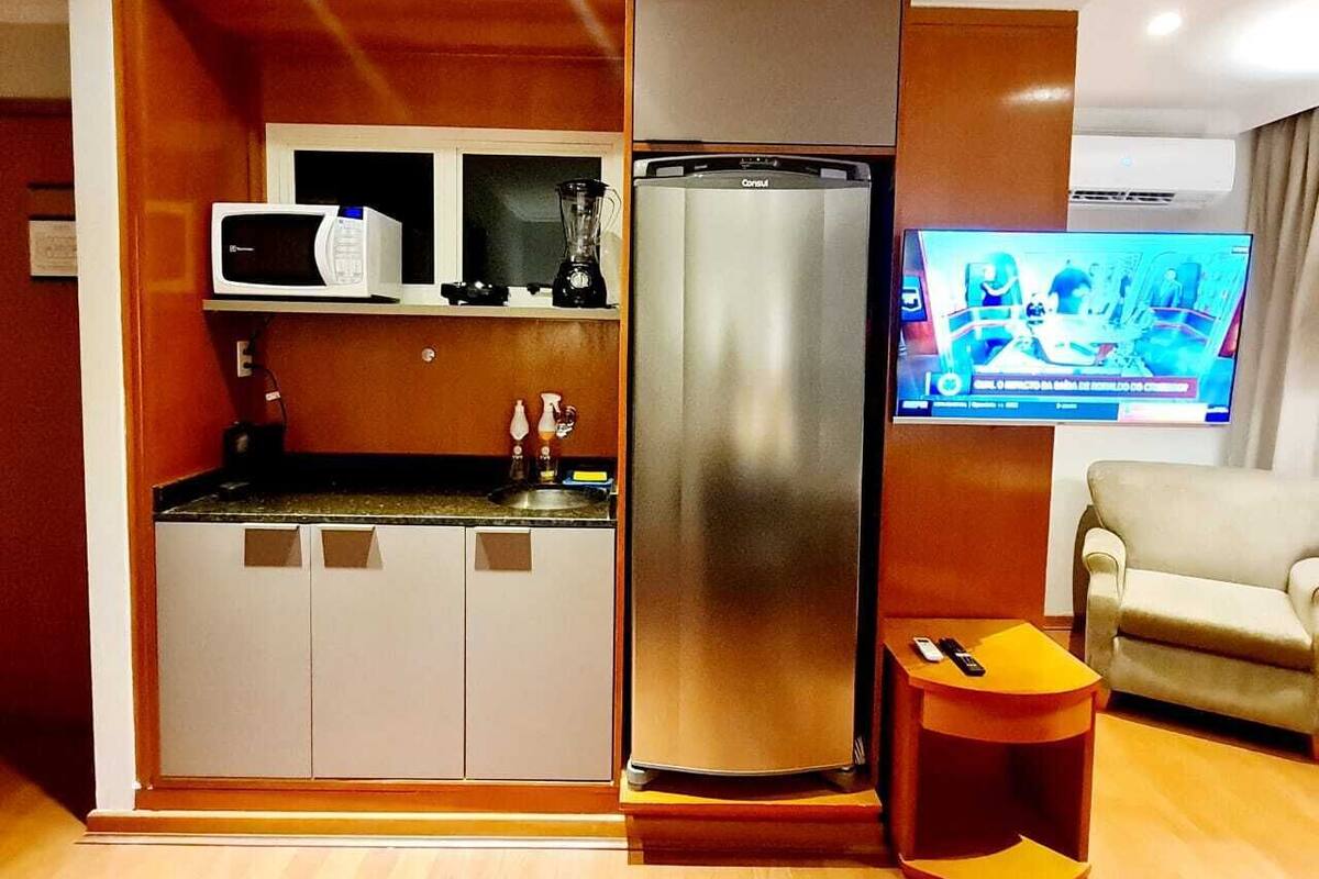 A compact living space with a kitchenette, a refrigerator, a flat-screen TV, and a sofa.