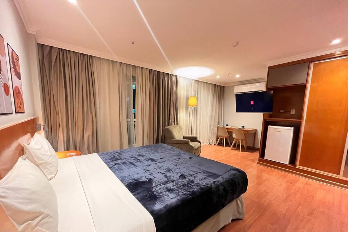 A hotel room with a bed, a desk, a chair, a television, and a wardrobe.