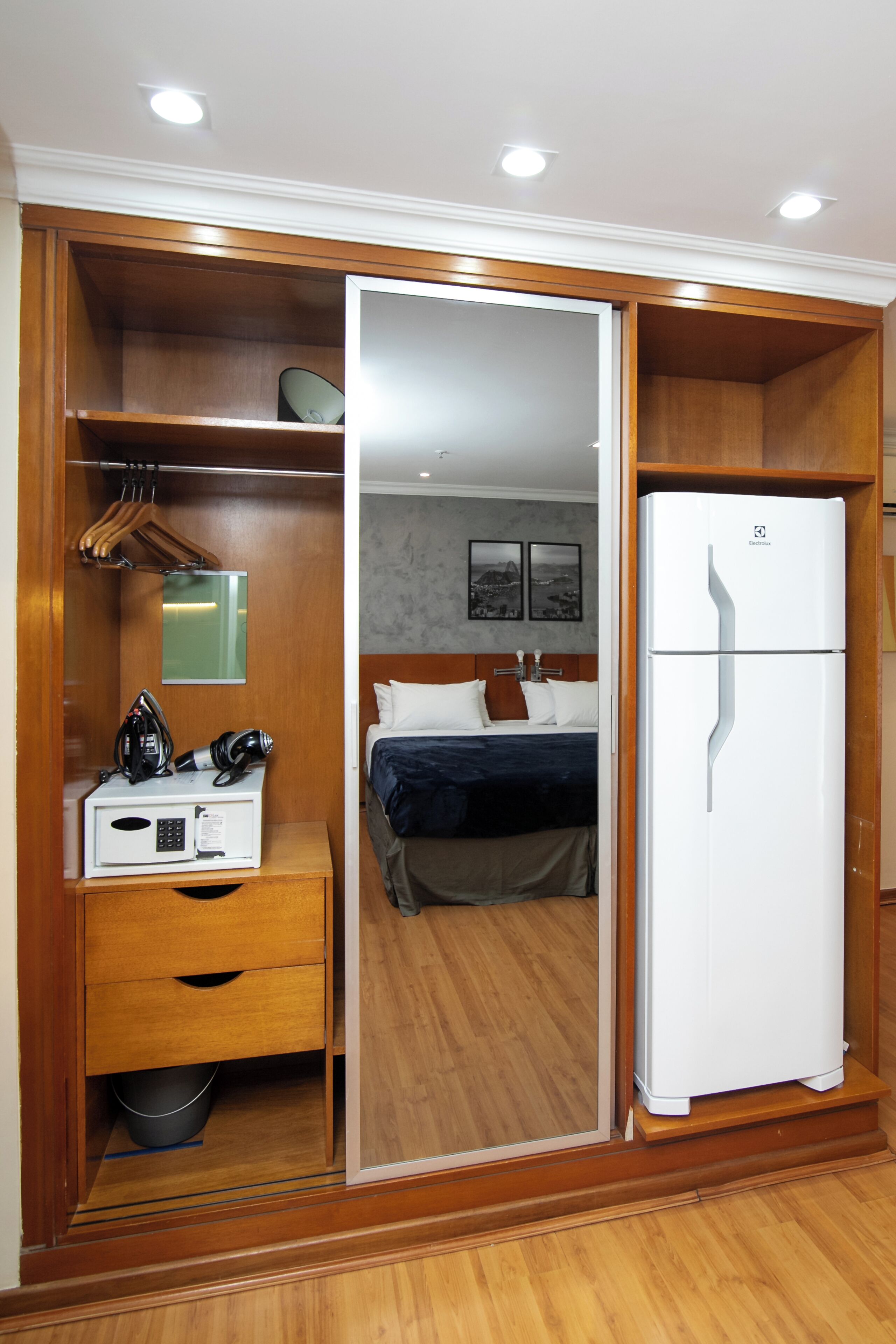 Ein Hotelzimmer mit einem Holzkasten, einem Bett mit Kissen, einem weißen Kühlschrank und einer Mikrowelle auf einem Nachttisch aus Holz.