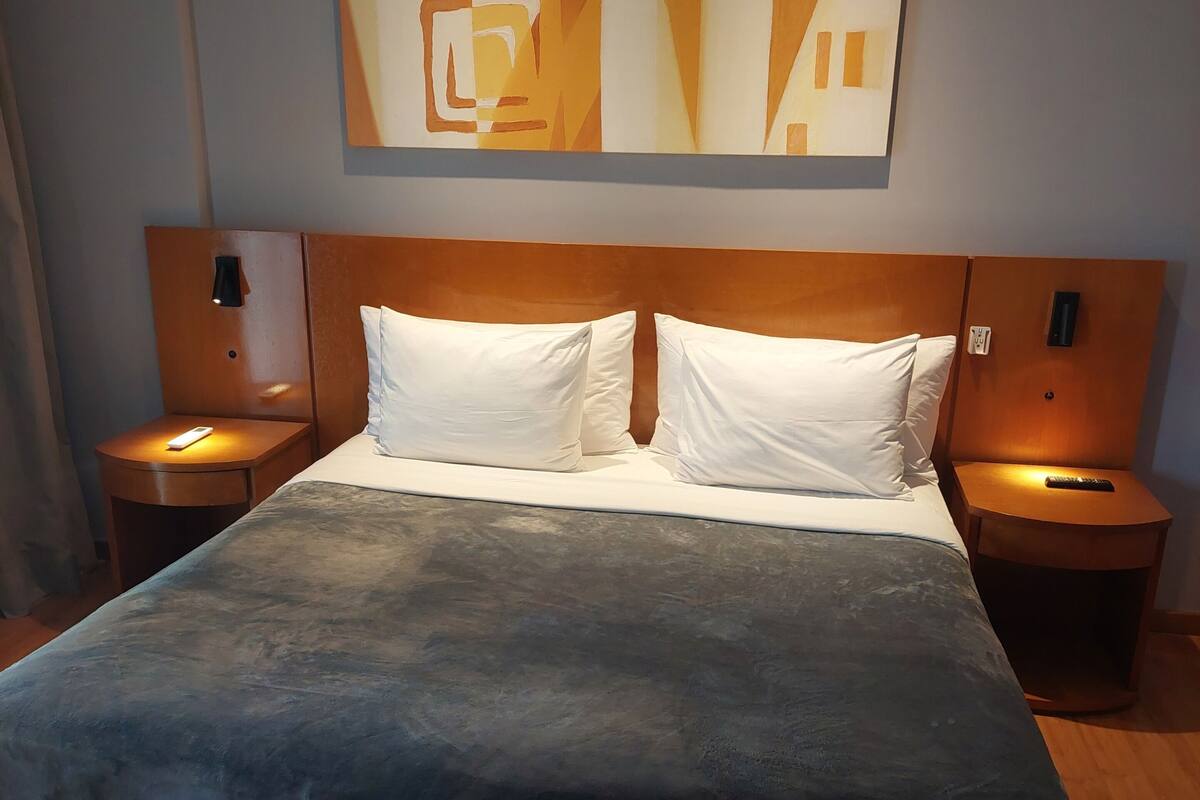 A hotel room with a large bed, two bedside tables, a nightstand, a wall-mounted artwork, and a wooden headboard.