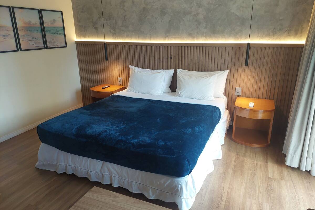 A hotel room with a bed, wooden headboard, bedside tables, and a wall-mounted light fixture.