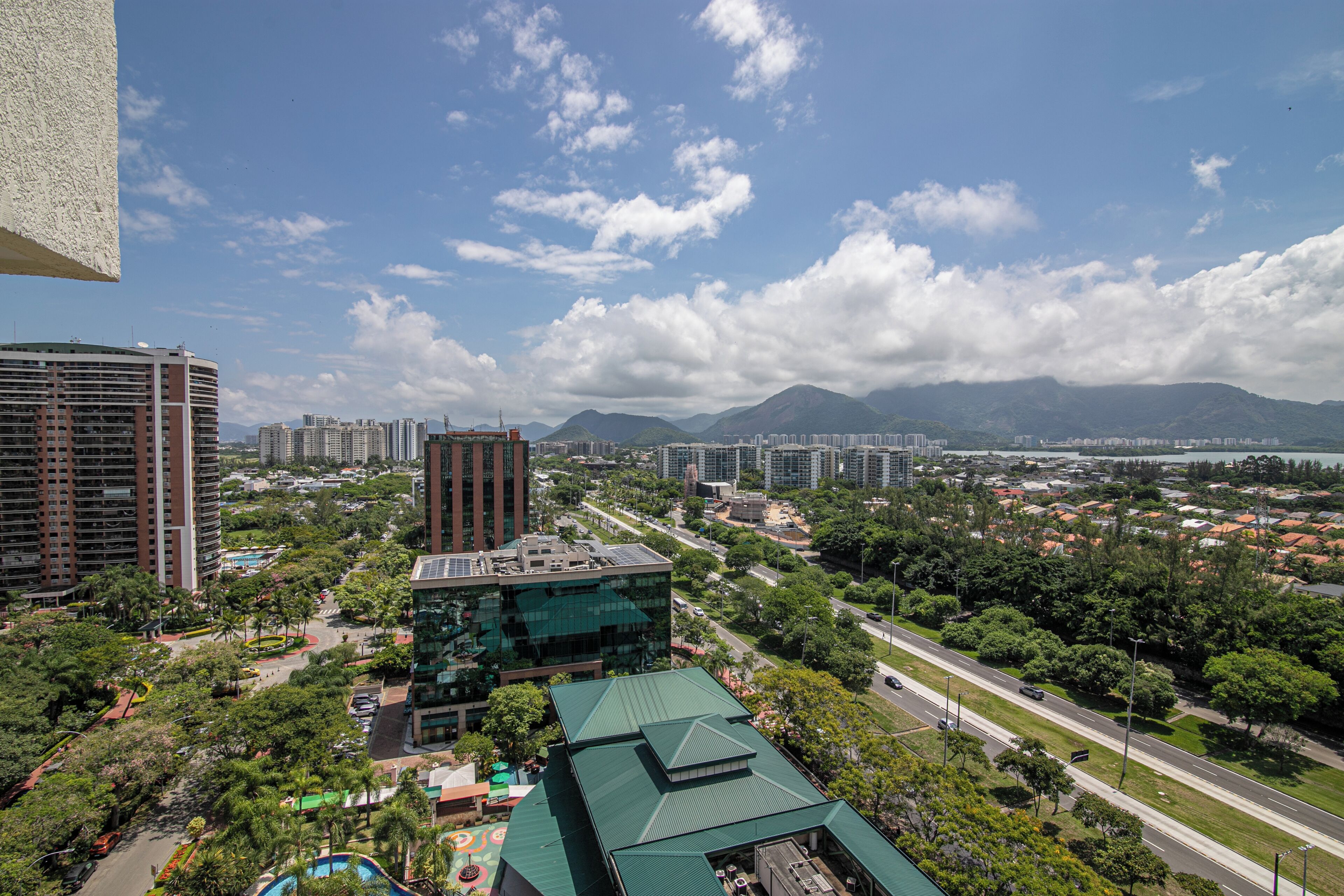 A high-rise building with a modern glass facade, surrounded by lush greenery and a clear blue sky.