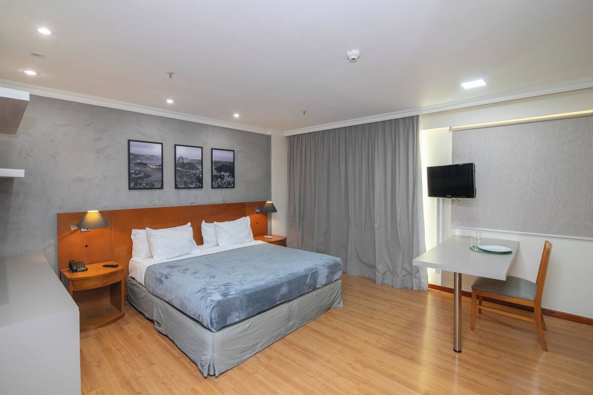 A hotel room with a bed, a desk with a chair, a television, and a wall-mounted TV.